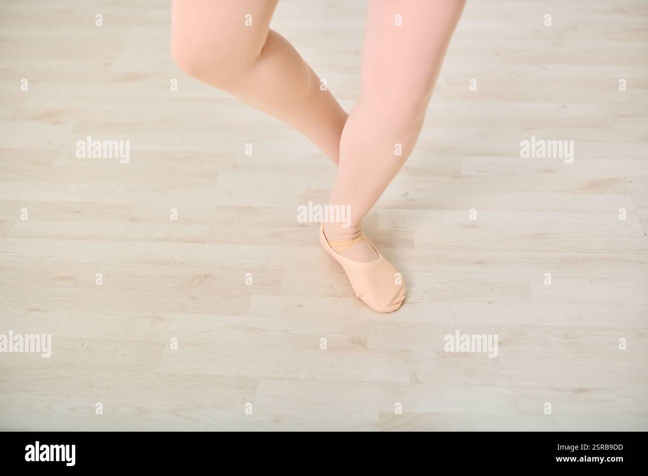 Nahaufnahme junger weiblicher Ballerinas-Beine während der Tanzprobe im Atelier. Holzboden und warme Beleuchtung heben die präzise Fußpositionierung während der Übung hervor Stockfoto