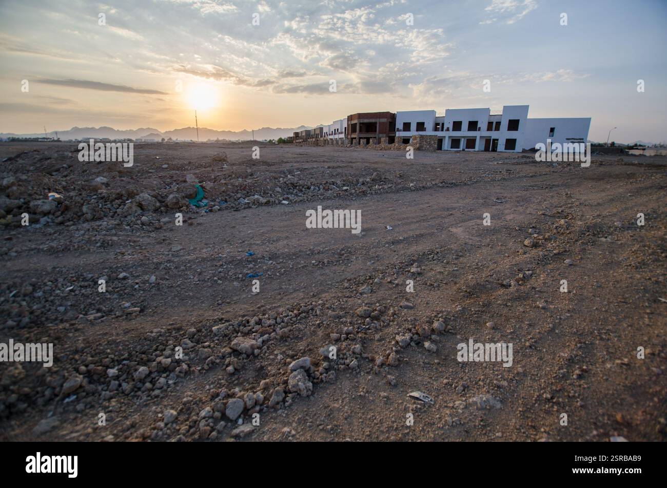 Wüstenhotel im Bau, in warmes Sonnenuntergangslicht getaucht. Raues Gelände umgibt das Gebäude mit verstreuten Wolken, die den Himmel noch tiefer machen. Umfangreich Stockfoto