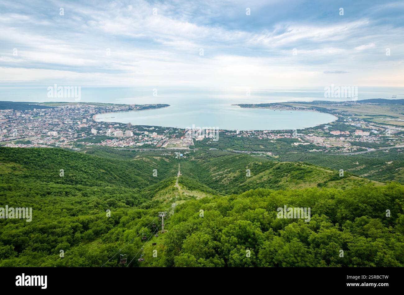 Die weitläufige Vogelperspektive zeigt die Bucht von Gelendschik mit üppigem Grün im Vordergrund. Die von Hügeln umgebene Stadtlandschaft ist deutlich unter bewölktem Himmel zu sehen. Se Stockfoto
