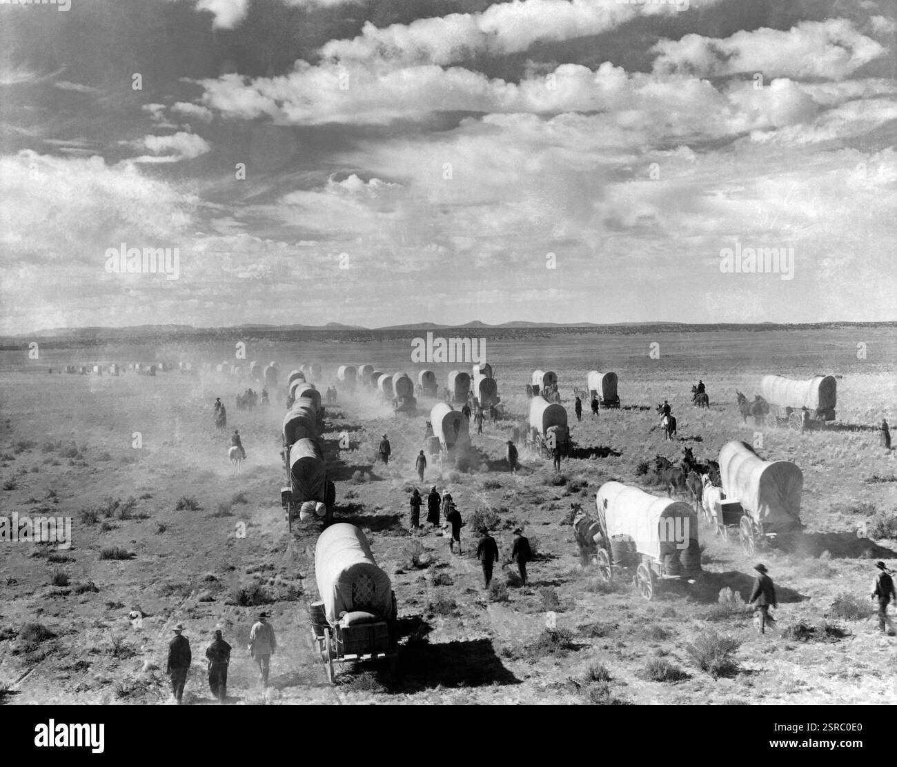 Lange Schlange von überdachten Wagen einige Leute gehen zu Pferd, während Horden von Menschen durch die Great Plains der USA fahren Stockfoto