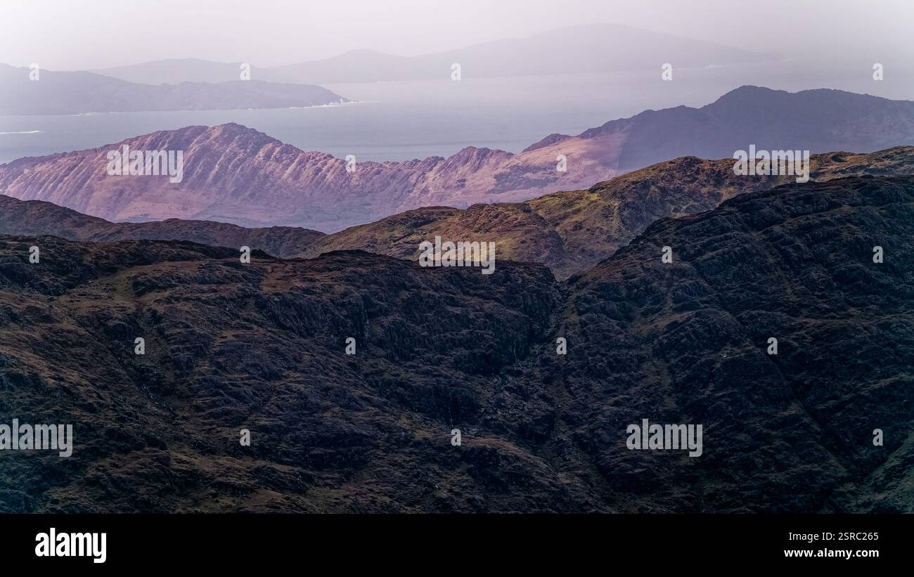 Zerklüftete Bergketten erstrecken sich im Vordergrund und bieten eine ruhige Küste und sanfte Hügel im Hintergrund unter hellem Mittagssonnenlicht. Stockfoto