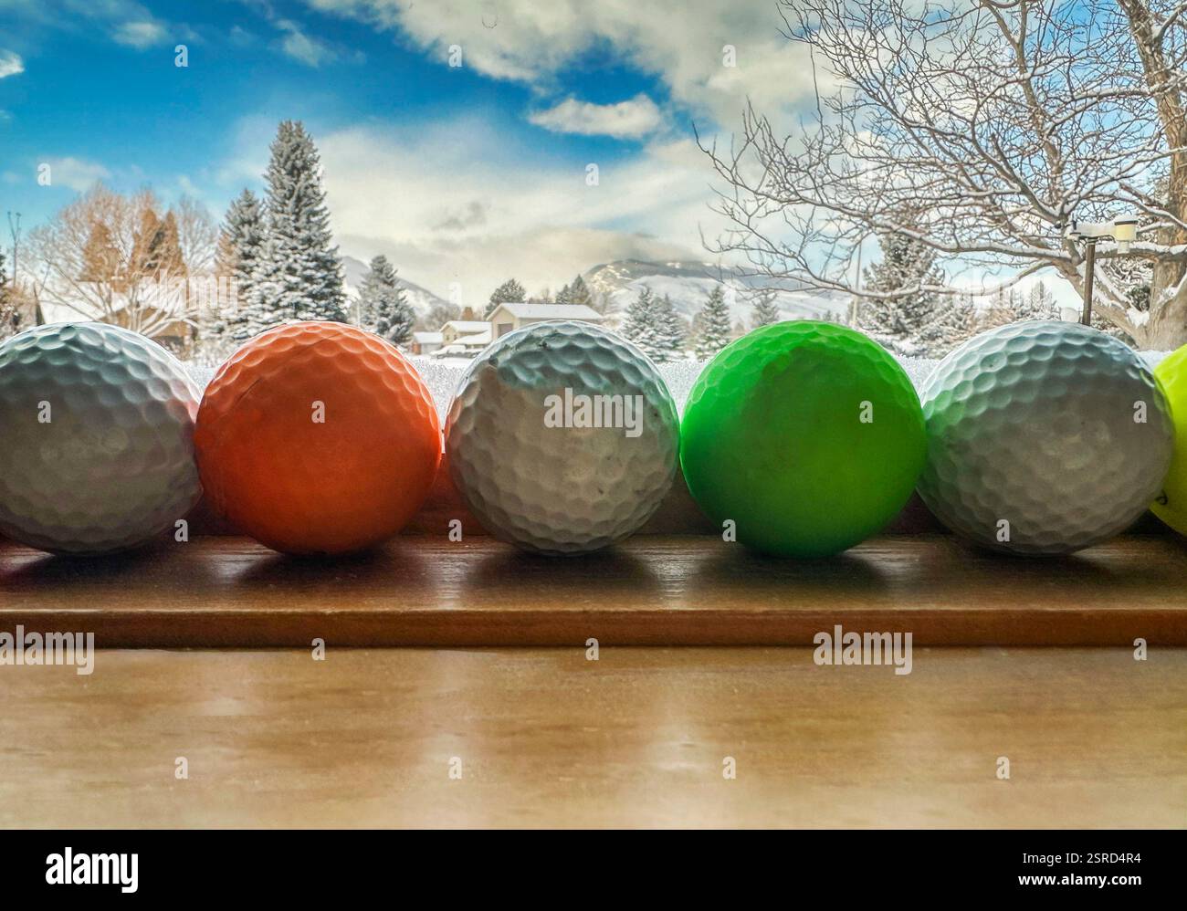 Golfbälle auf der Fensterbank bieten einen gerahmten Blick auf die Schneelandschaft mit Kiefern, Bergen, blauem Himmel und Wolken. Der Golfplatz liegt im Vordergrund und im Schnee. Stockfoto