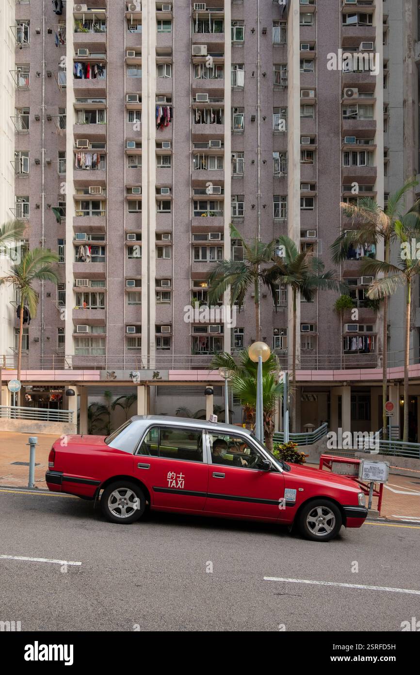 Ein rotes Taxi parkte in der Tin Wan New Street vor dem Hung Fuk Court, einem modernen Wohnhochhaus in Aberdeen, Hongkong, umgeben von Palmen. Stockfoto Ein rotes Taxi parkte in der Tin Wan New Street vor dem Hung Fuk Court, einem modernen Wohnhochhaus in Aberdeen, Hongkong, umgeben von Palmen. Stockfoto