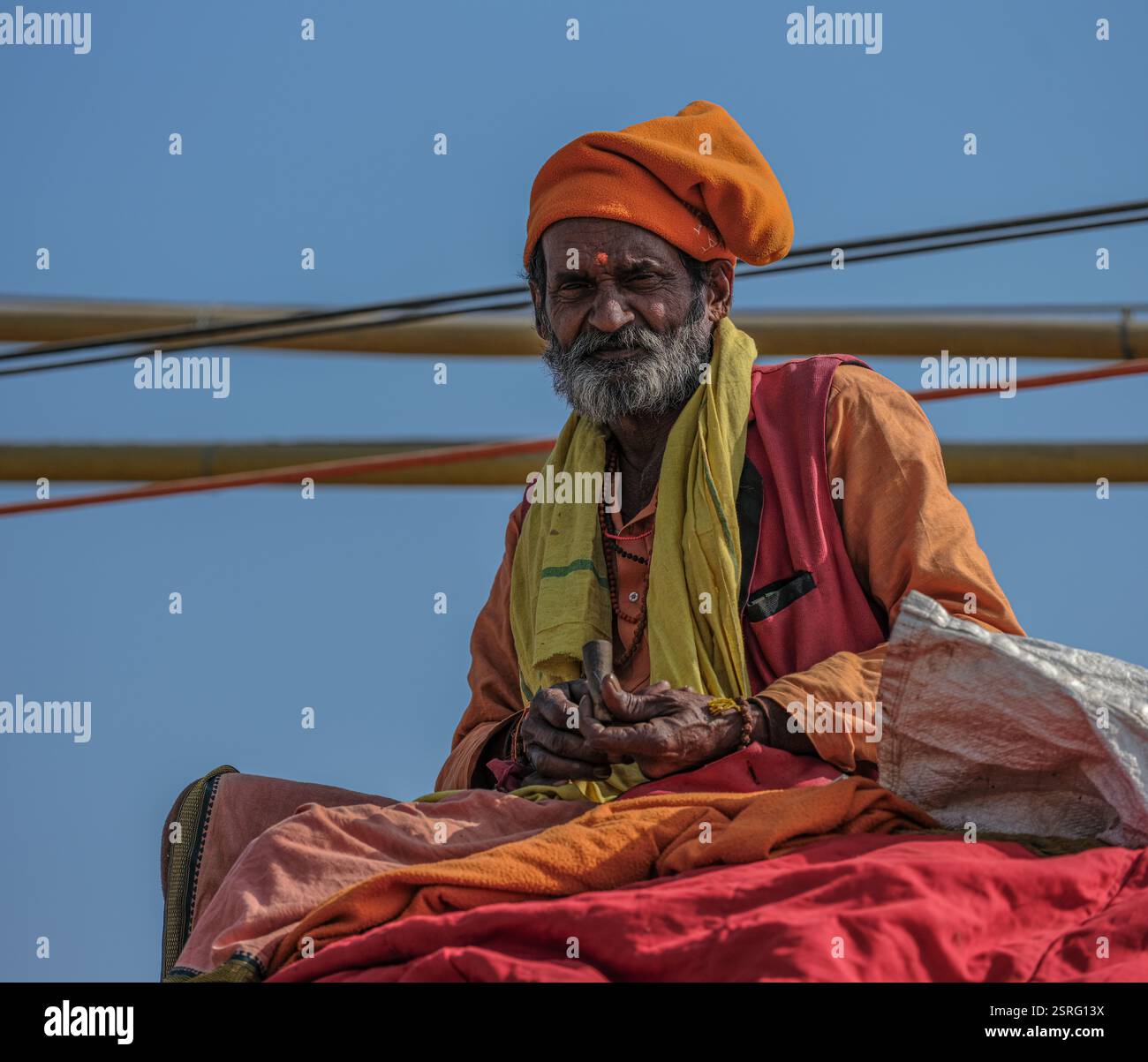 Ein hinduistischer Sadhu in traditioneller orangener Kleidung sitzt auf einem Elefanten und raucht während der Maha Kumbh Mela in Prayagraj, Indien, ein Chillum. Stockfoto