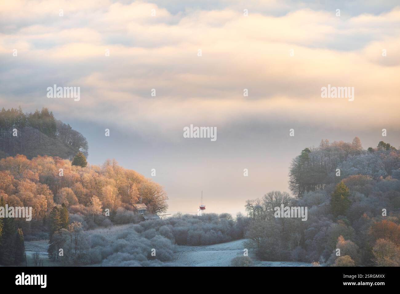 Ein einsames Segelboot auf einem ruhigen nebeligen See von Windermere mit wunderschönem Winterlicht. Lake District, Großbritannien. Stockfoto