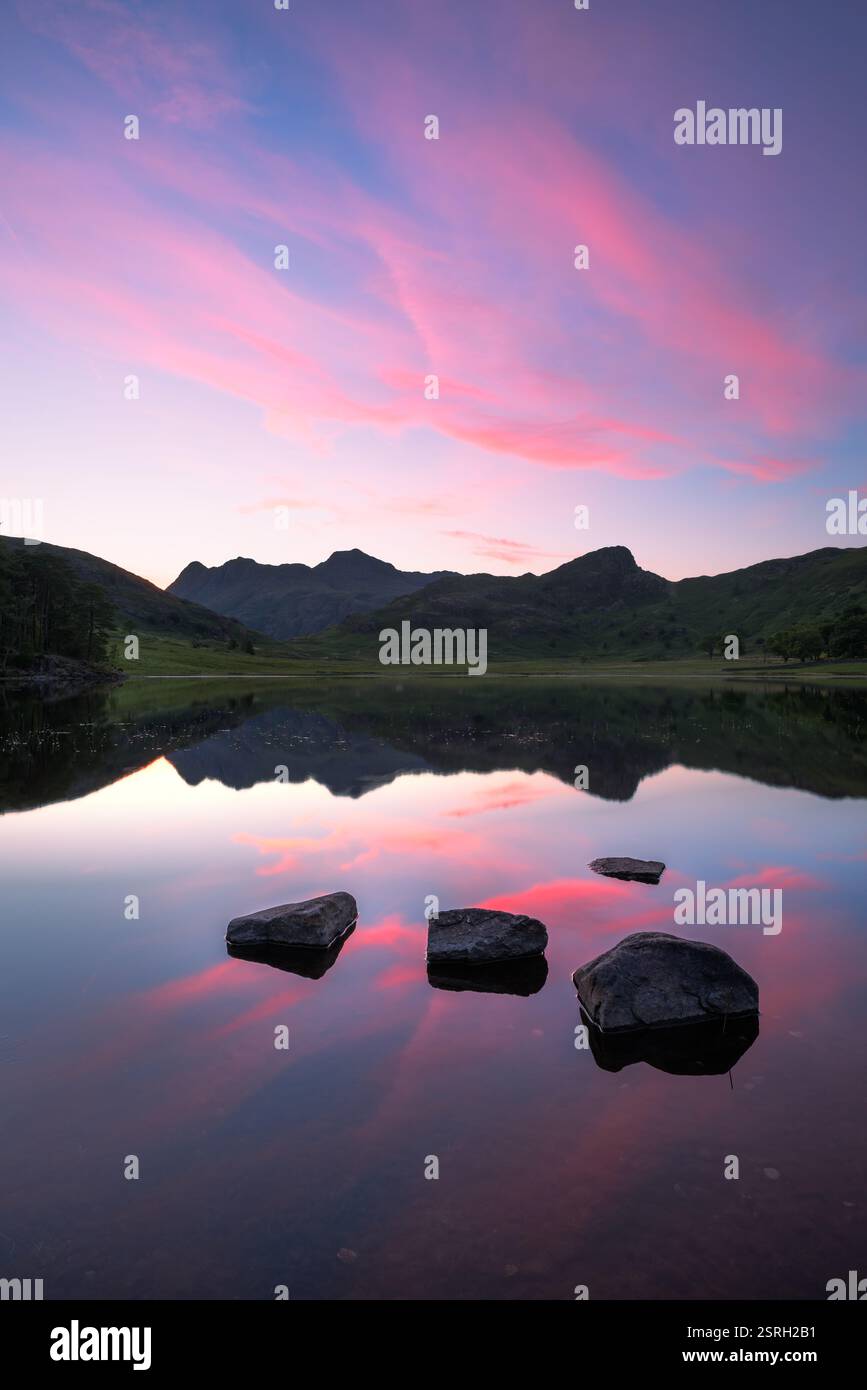 Wunderschöner Sommersonnenuntergang mit Felsen im Wasser am Blea Tarn im Lake District, Großbritannien. Stockfoto