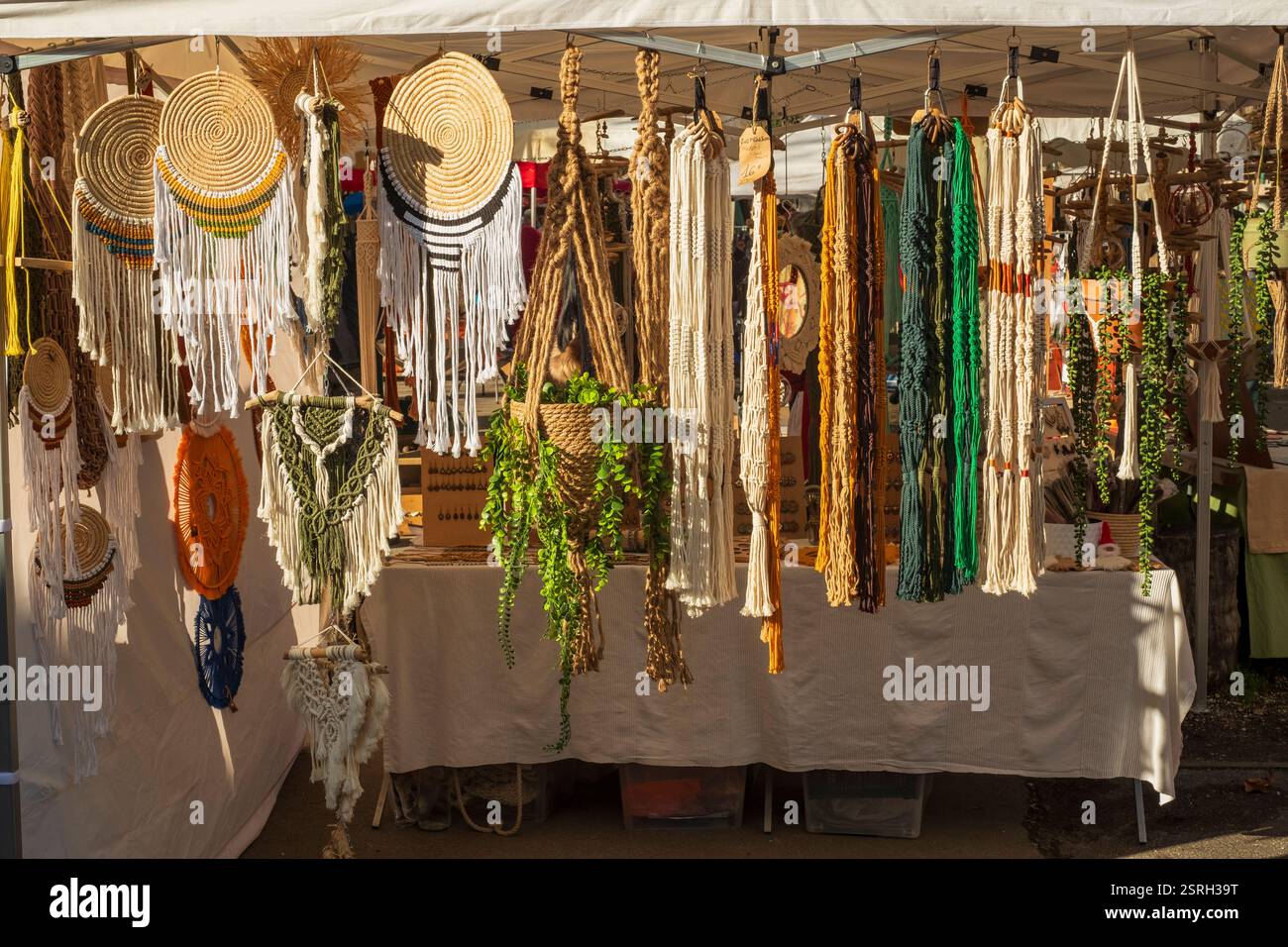 Ein Marktstand im Freien in Montbrun-Bocage, Frankreich, der handgefertigte Gestrick- und Makramee-Dekorationsgegenstände wie Pflanzenhalter und Wandbehänge präsentiert. Stockfoto