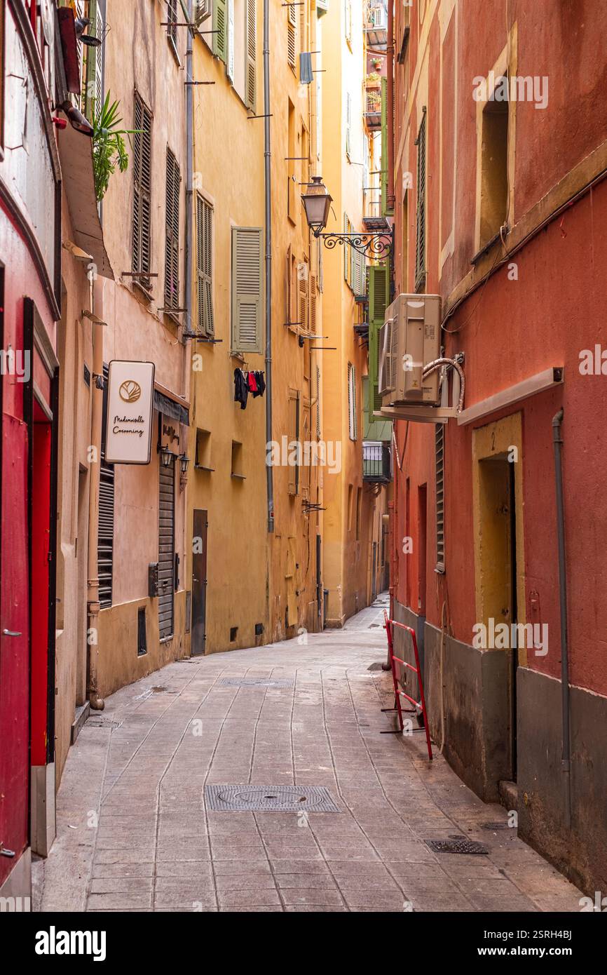 Leere, schmale Gasse in Nizza, Frankreich, mit sanftem Winterlicht und lebhaften historischen Gebäuden, die zum Erkunden und Entspannen einladen. Stockfoto