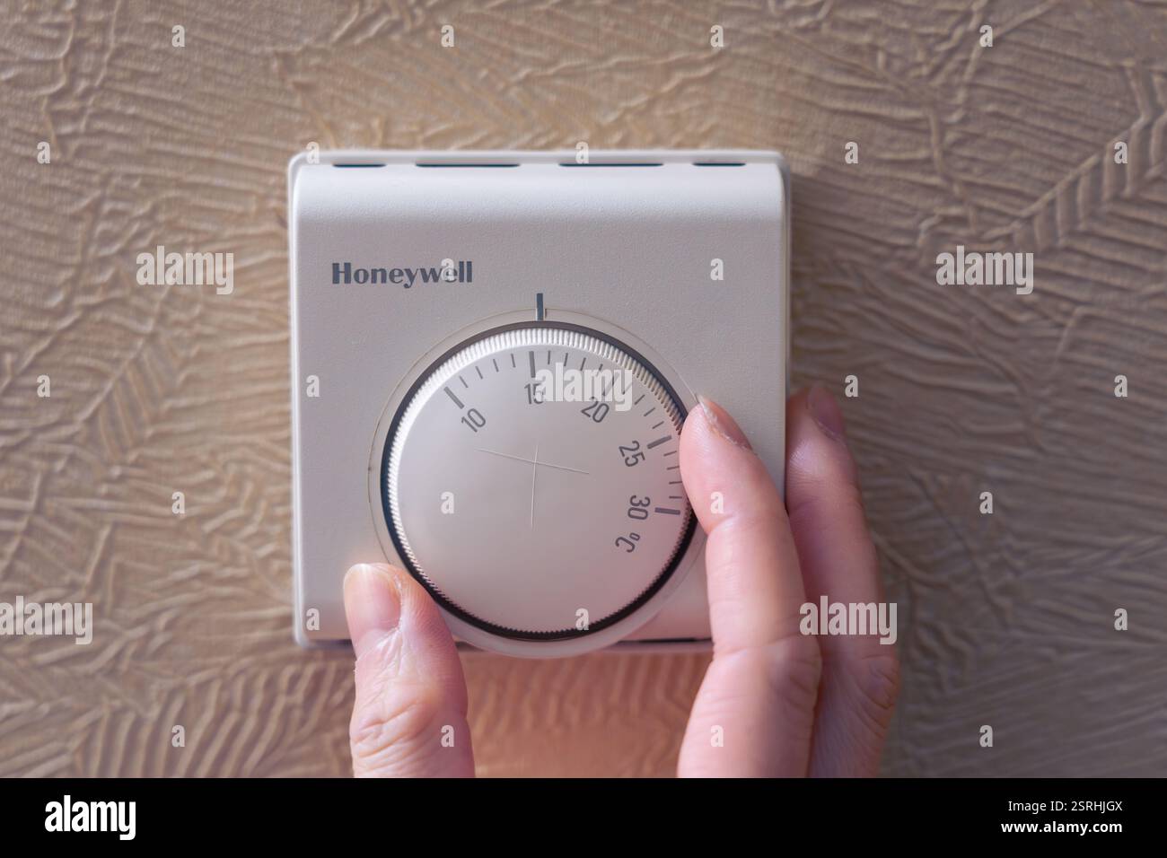 Eine Frauenhand, die einen Temperaturregler an einem Honeywell Thermostat in einem Haus in England dreht. Konzept: Zentralheizung, Energierechnungen, Energiehöchstgrenze, Gaspreis Stockfoto