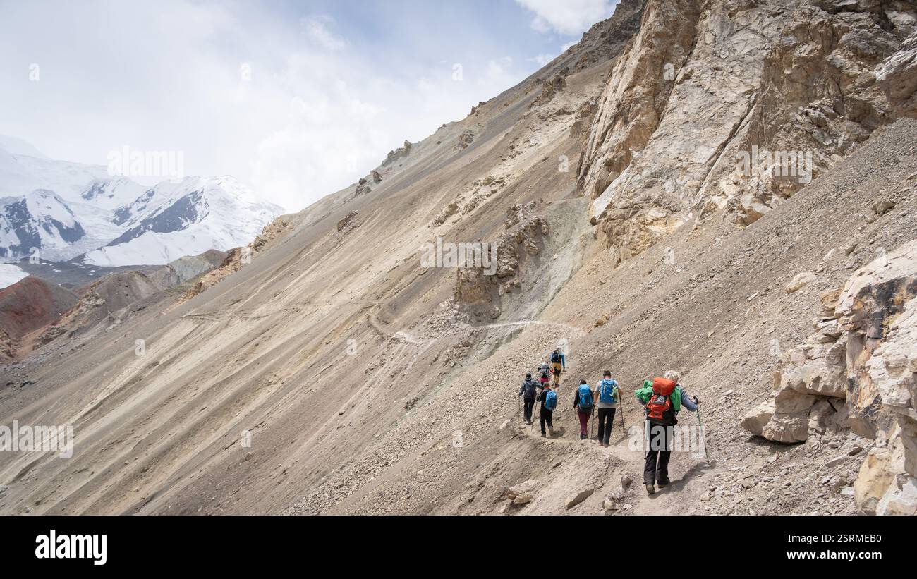 Touristen wandern Geröll auf der Seite des Berges mit schneebedecktem Hintergrund, Pamir Berge, Kirgisistan Stockfoto