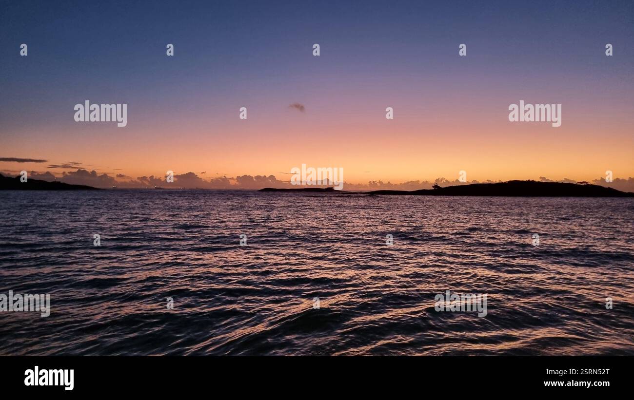 Die Sonne blickt direkt über dem Horizont, strahlt strahlendes goldenes Licht über den Himmel und spiegelt sich wunderschön auf dem plätschernden Wasser. - Smartphone-aufgenommenes Stockfoto