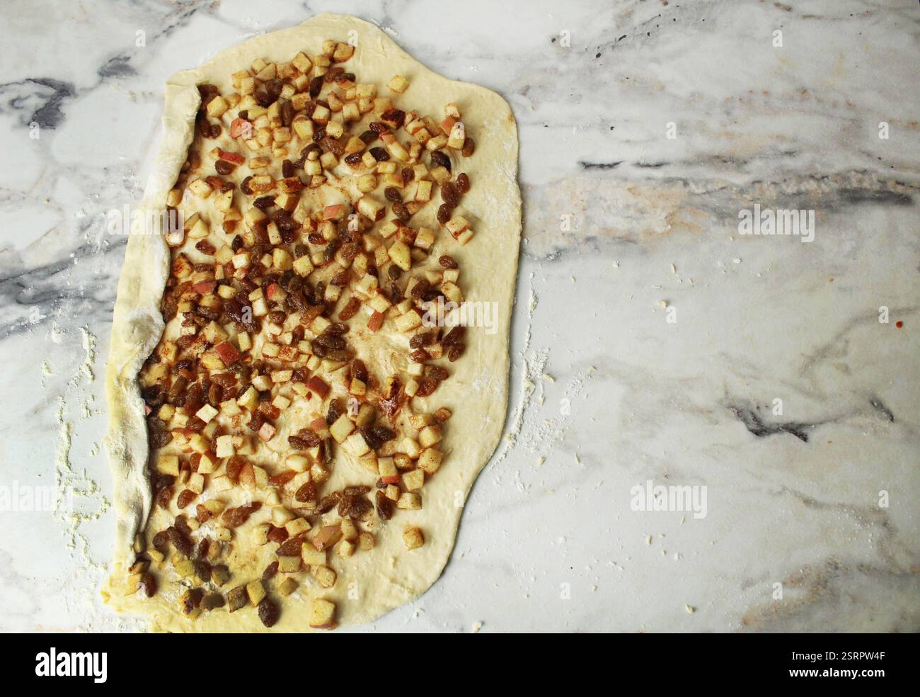 Wickelt eine Schicht Hefeteig gefüllt mit Apfel und Rosinen in ein Brötchen. Platz für Text im Copyspace. Stockfoto