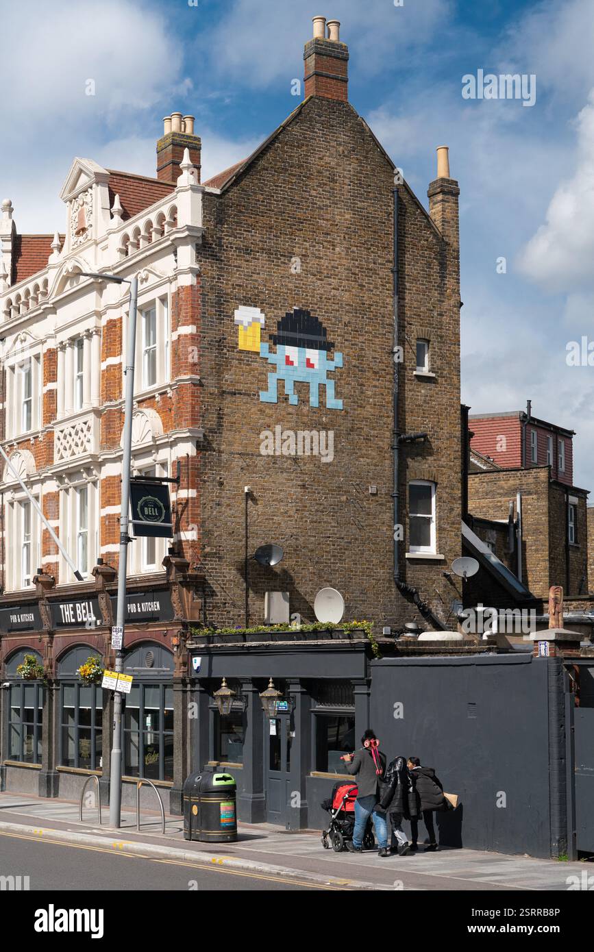 Pixelated Space Invaders Wandgemälde im Bell Pub, einem Pub und einer Küche in London, Großbritannien. Leute gehen vorbei. Stockfoto
