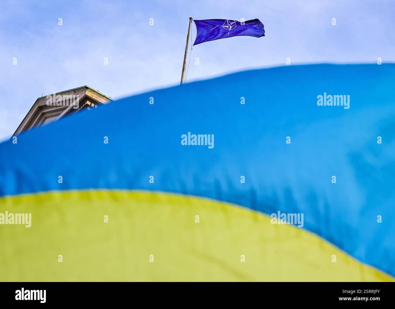 London, Großbritannien. Februar 2025. Die Flagge, die hinter der Ukraine zu sehen ist, ist von einem nahe gelegenen proukrainischen Protest gegenüber der Downing Street gekennzeichnet. Die NATO-Flagge wurde heute im Verteidigungsministerium gehisst und fliegt. In den letzten Tagen waren Veranstaltungen und Reden auf der Münchner Sicherheitskonferenz, die heute endet, ein viel diskutiertes Thema, einschließlich Meinungsverschiedenheiten über eine künftige NATO-Mitgliedschaft der Ukraine. Die europäischen Regierungschefs werden morgen in Paris zu einem Dringlichkeitsgipfel zusammentreten, auf dem die Verteidigung und die europäische Sicherheit ganz oben auf der Tagesordnung stehen dürften. Stockfoto