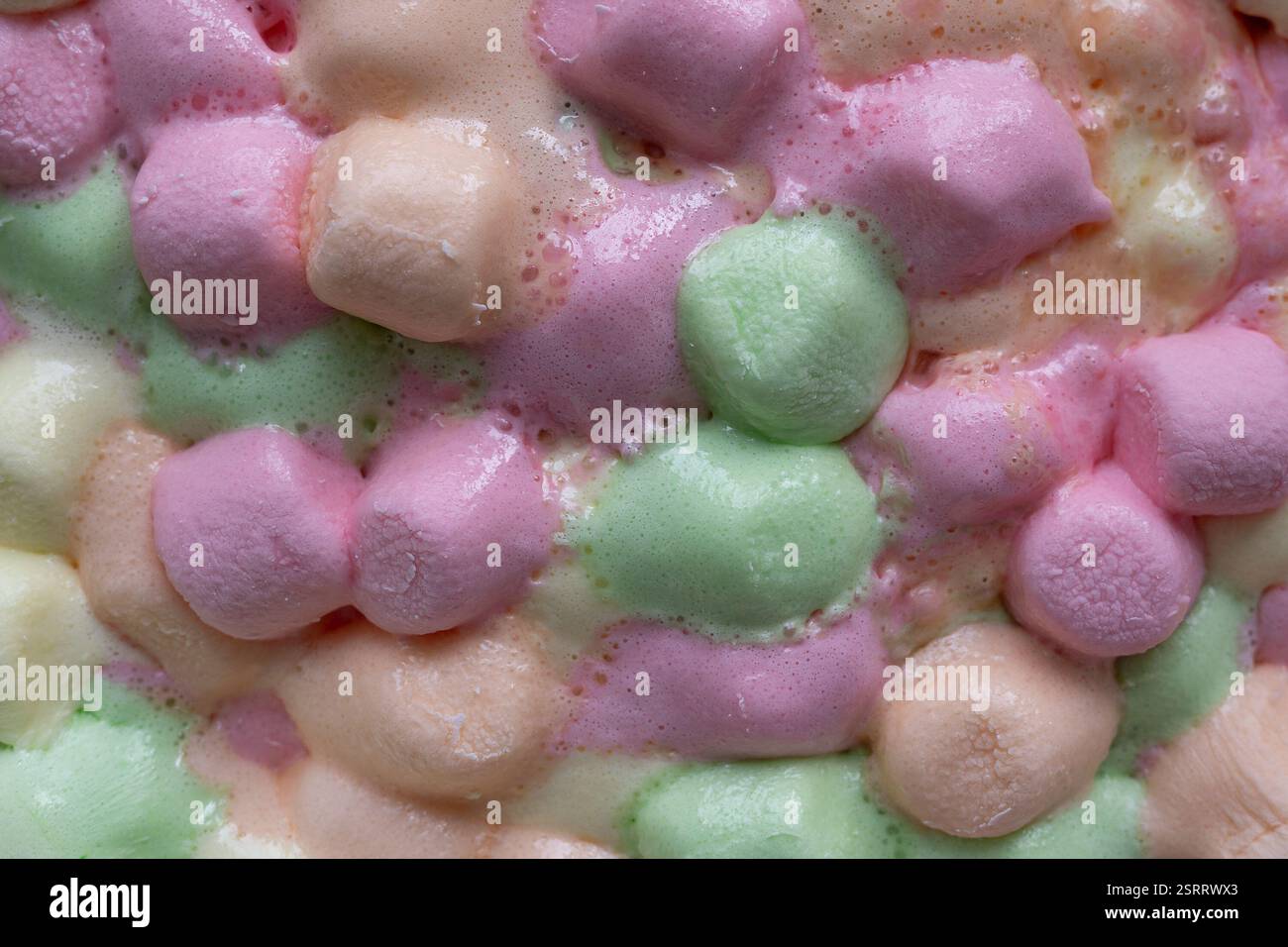 Eine köstliche Mischung aus pastellfarbenen Marshmallows, die in einer Glasschale schmelzen und eine weiche Farbexplosion und eine flauschige Textur erzeugen. Stockfoto