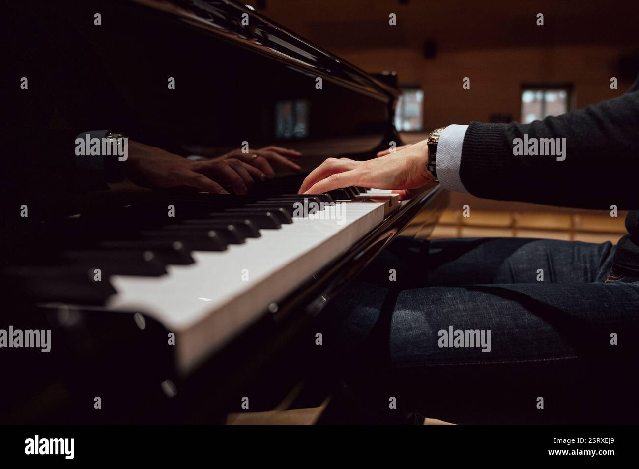 Eine Nahaufnahme der Hände eines Pianisten, die einen Flügel spielen, mit Reflexionen auf der glänzenden Oberfläche. Der schwach beleuchtete Konzertsaal unterstreicht die intime Atmosphäre und Kunst Stockfoto