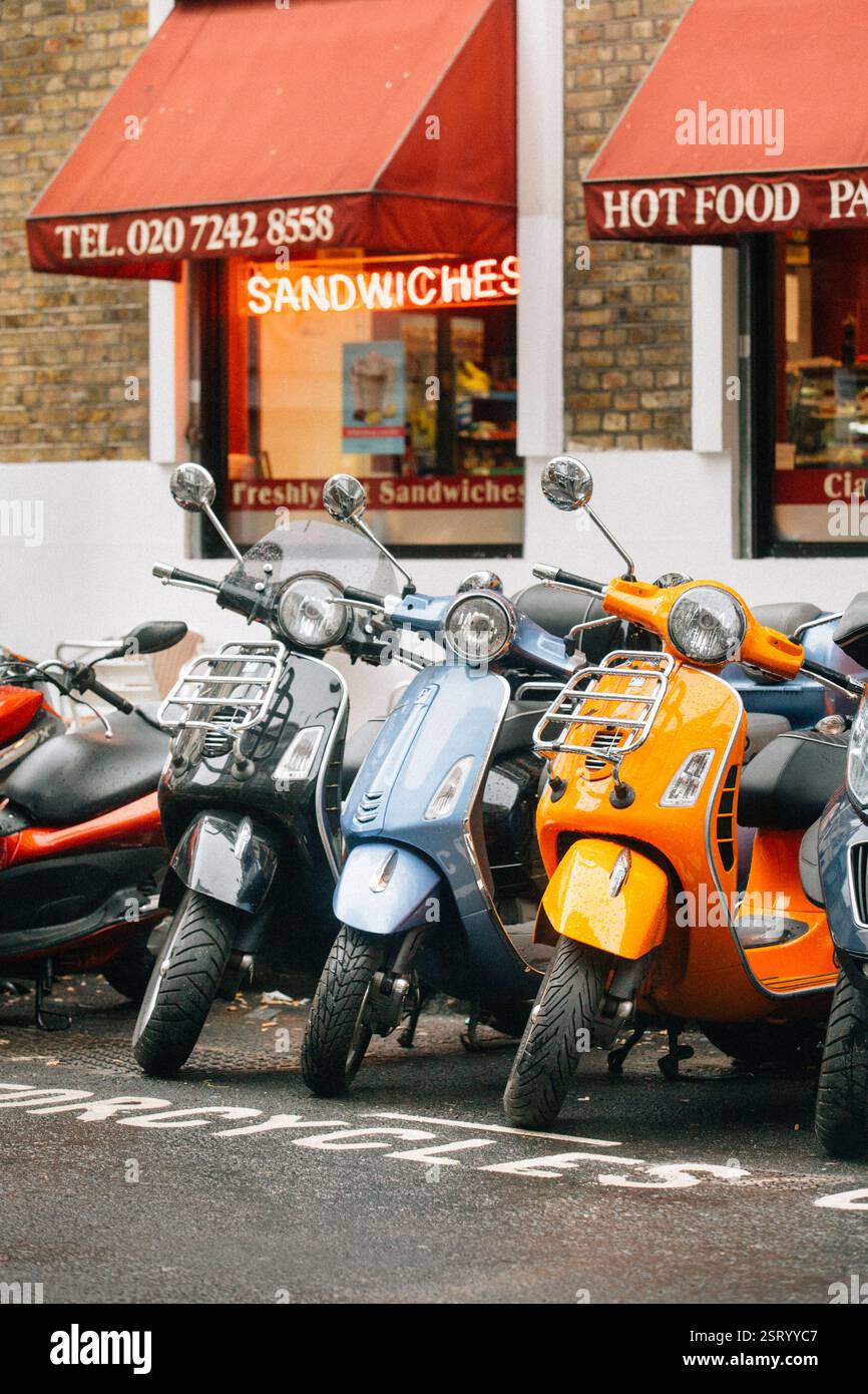 Vespas parkten vor einem Sandwiches-Laden in London, wahrscheinlich in der Nähe eines Backsteingebäudes. Regnerischer Tag. Stockfoto
