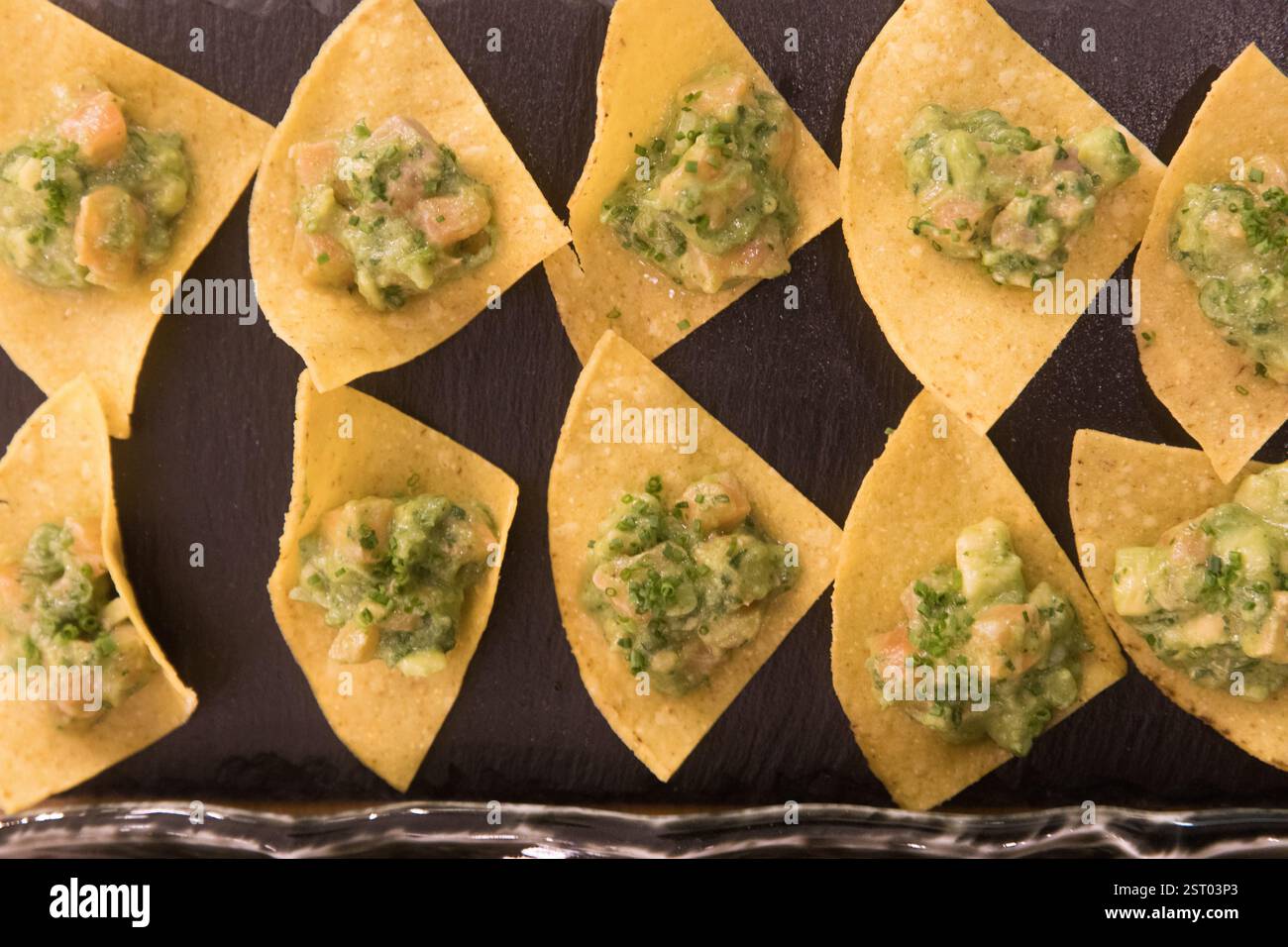 Kleine, dreieckige Tortilla-Chips mit Guacamole und Lachs Stockfoto