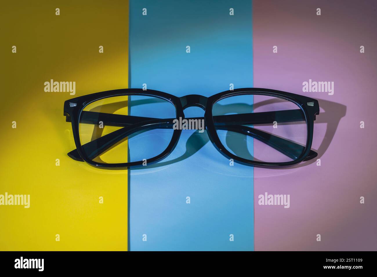 Schwarz gerahmte Brille auf einem leuchtenden geometrischen Hintergrund in Gelb, Blau und Rosa, die künstlerische Schatten wirft. Moderne konzeptuelle Bildrepresentin Stockfoto