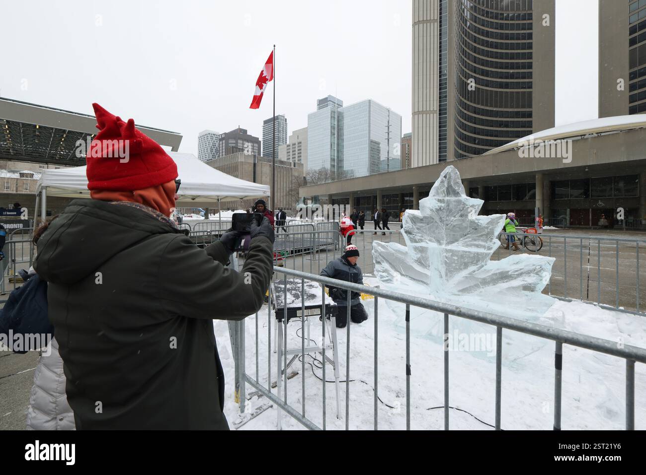 Toronto, Kanada, 15. Februar 2025. Ein Eisbildhauer schuf am 15. Februar 2025 eine Ahornblatt-Eisskulptur unter einer riesigen kanadischen Flagge auf dem Platz der Toronto City Hall in Toronto, Kanada. Am 15. Februar wurde vor dem Rathaus eine riesige kanadische Flagge mit einer Länge von 30 Metern und einer Breite von 15 Metern gehisst, um den 60. Jahrestag der Einweihung der kanadischen Flagge zu feiern. Quelle: Yu Ruidong/China News Service/Alamy Live News Stockfoto