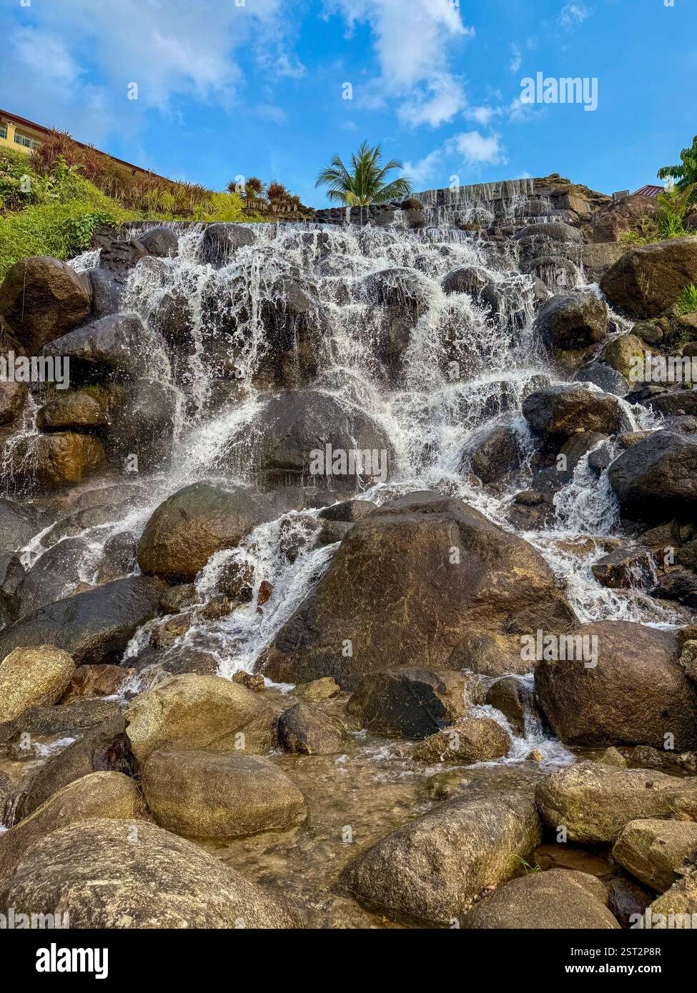 Stepped Waterfall Over Rocks2 Ein mehrstufiger Wasserfall, der über große Felsen kaskadiert und von üppigem tropischem Grün umgeben ist. Das klare Wasser fließt gleichmäßig - Smartphone-aufgenommenes Stockfoto