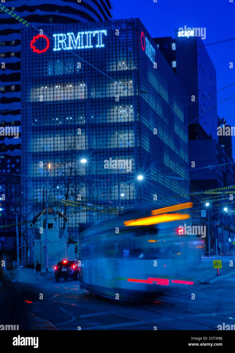 Das Gebäude 100 der RMIT University (Design Hub) in Melbourne, Australien, wurde bei Dämmerung mit einer vorbeifahrenden Straßenbahn erfasst Stockfoto
