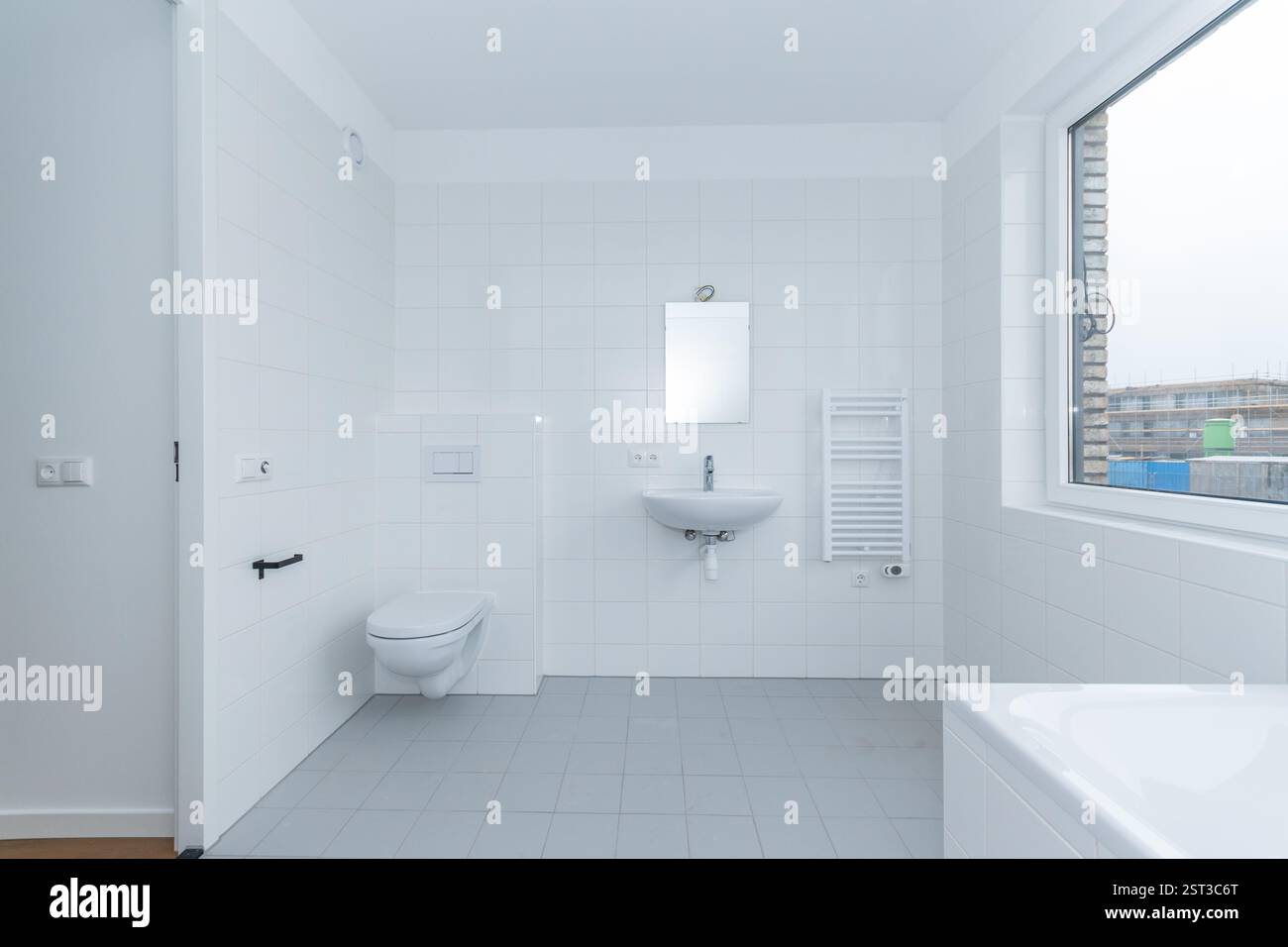 Innen sauberes, weiß gefliestes Badezimmer mit Waschbecken, Toilette WC und Spiegel in einem modernen Neubau-Smart-Haus durch Fenster ist eine Weiterentwicklung Stockfoto