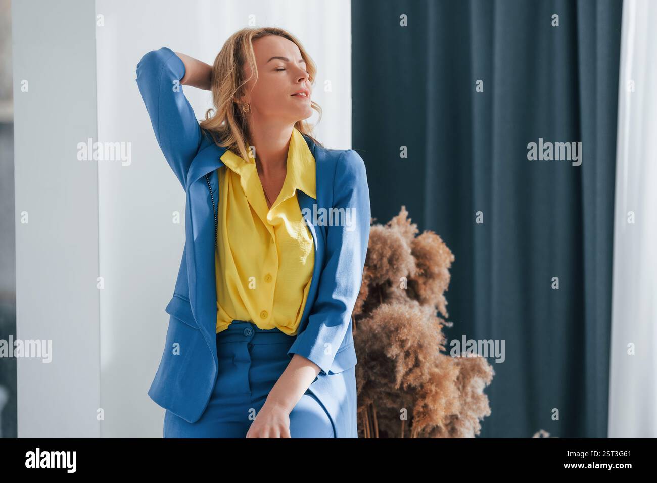 Frau in formellem blau-gelben Hosenanzug ist drinnen. Stockfoto
