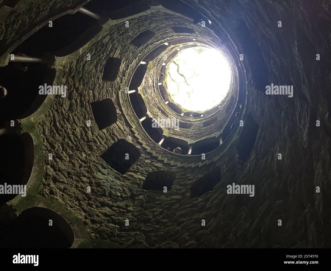 Eine Wendeltreppe führt zu einer hellen Öffnung. Steinmauern und unebene Stufen schaffen ein Gefühl von Mysterium. Sintra, Portugal. Symbolisch für Selbstfindung und Stockfoto