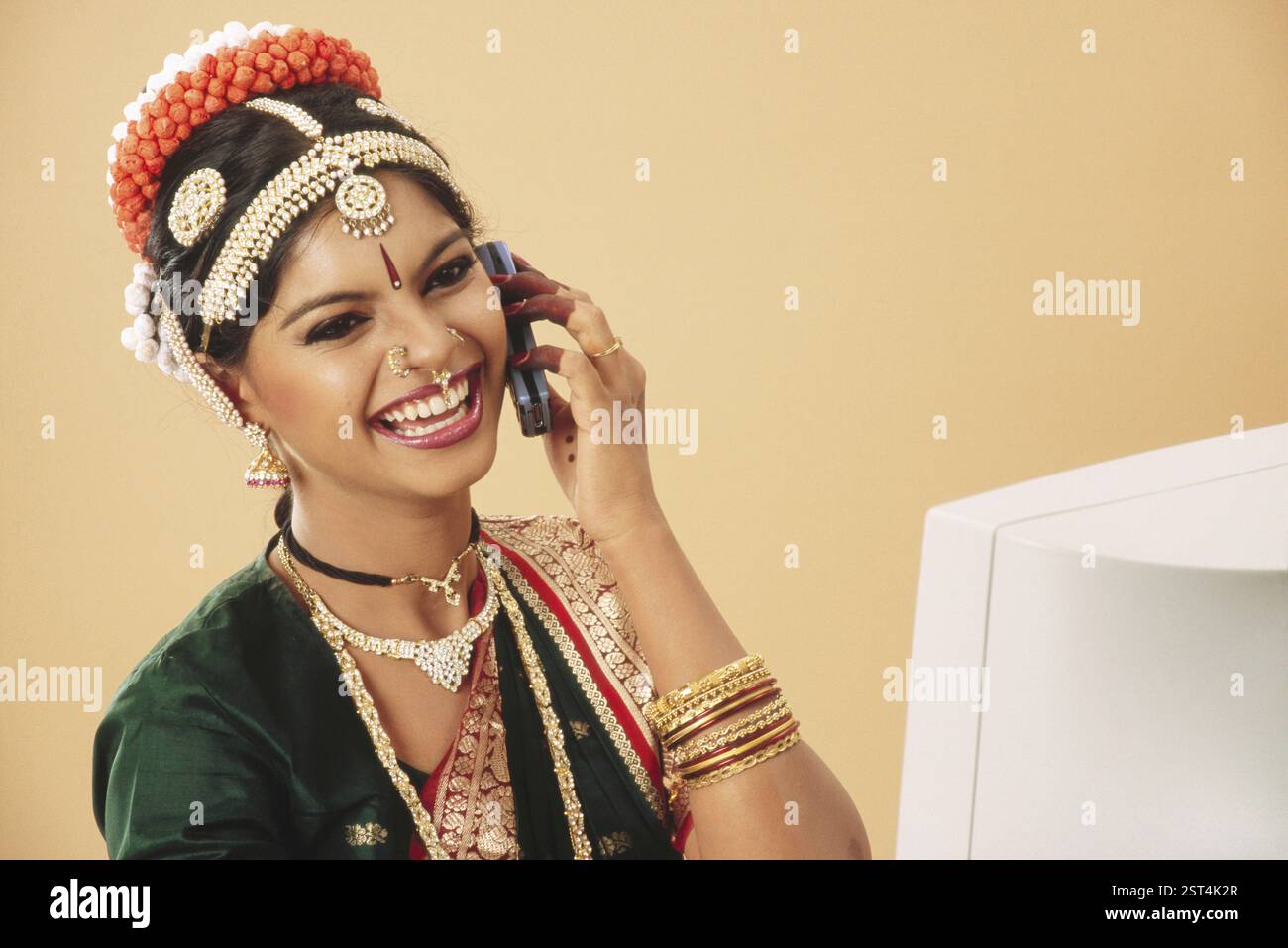 Südasiatische Indianerin, die auf dem Handy sitzt, vor dem Computer MR. 579 Stockfoto