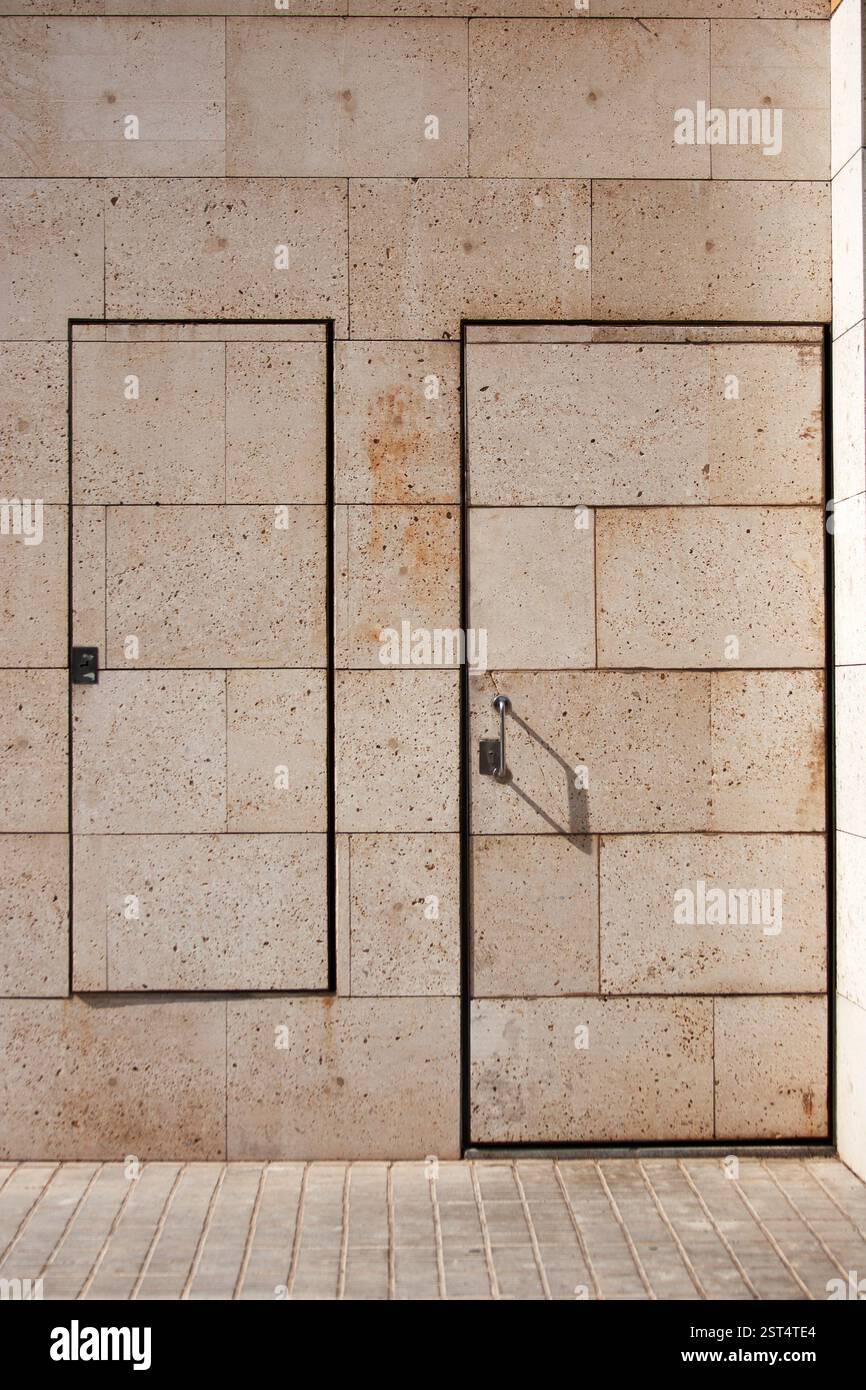 Ein minimalistisches architektonisches Design mit einer strukturierten beigefarbenen Steinwand mit zwei versteckten Türen, die sich nahtlos in das Muster einfügen. Stockfoto