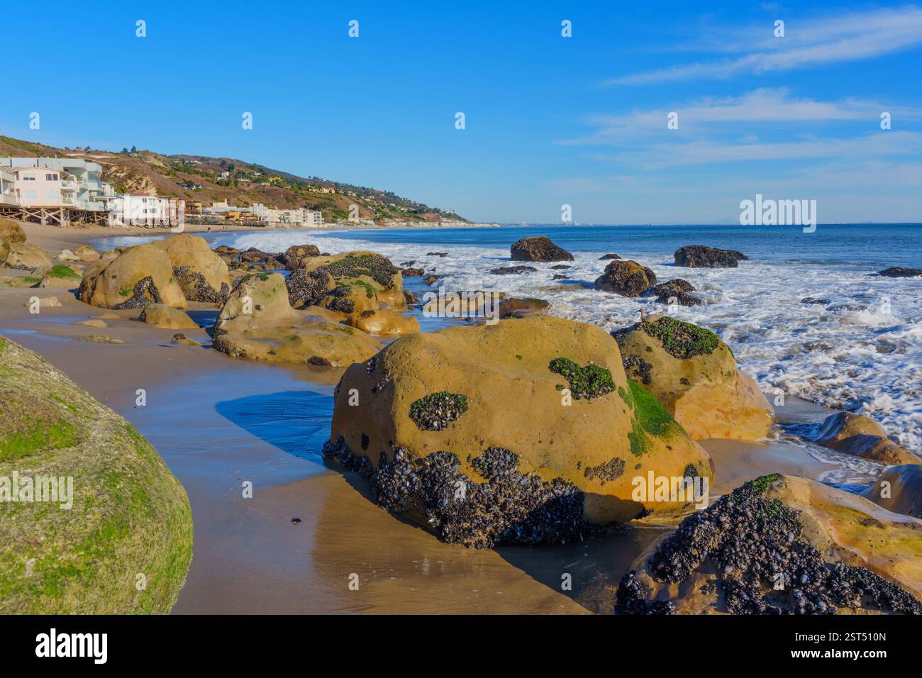 Große felsige Küste von Malibu Beach mit Häusern im Hintergrund vor einem klaren Himmel. Stockfoto