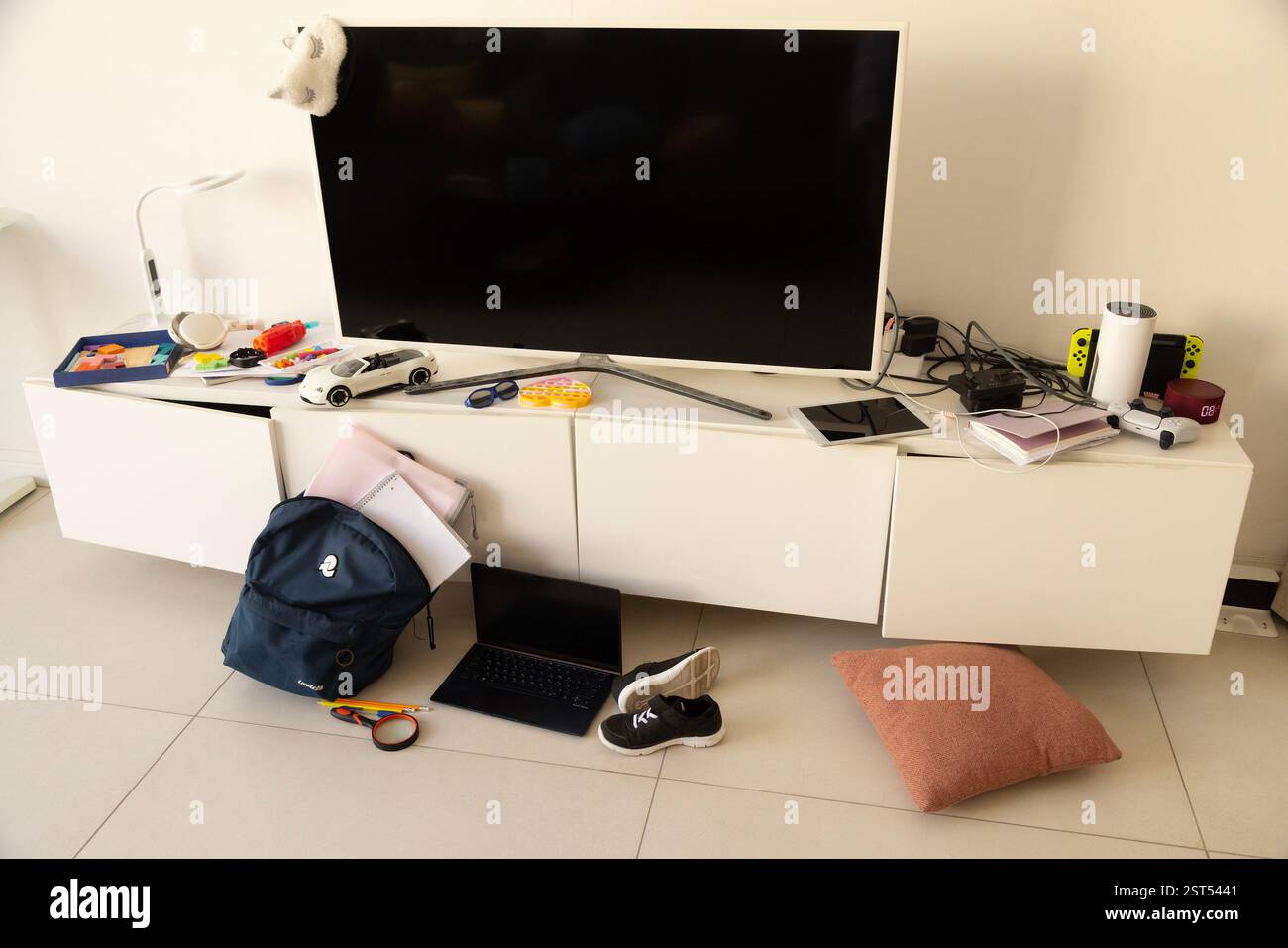 Ein unordentliches Wohnzimmer in der Nähe des Fernsehers mit Schultasche, Laptop, Büchern, Notizbüchern und Gadgets überall Stockfoto