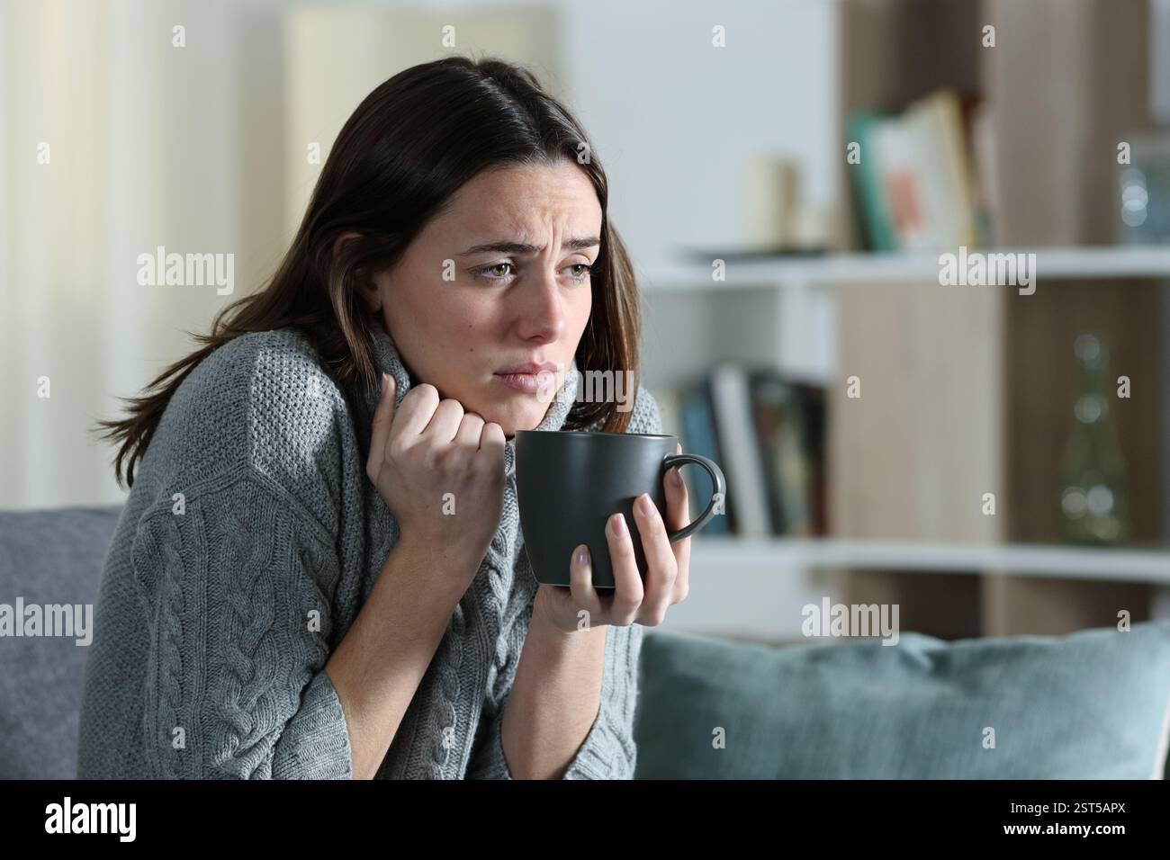 Kranke Frau, die kalt wird und Kaffee trinkt und sich im Winter zu Hause auf einer Couch beschwert Stockfoto