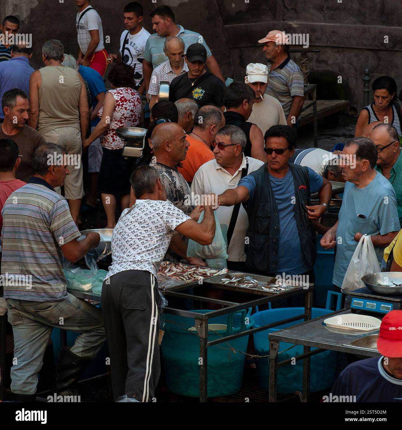 In der Tasche: Der Ständerhalter überreicht eine Tasche mit Meeresfrüchten an männliche Kunden in La Pescheria, dem belebten Open-Air-Fischmarkt in Catania, Sizilien, Italien. Der Markt wird sechs Tage die Woche gehandelt und zieht sizilianische Käufer an, die Fisch und andere frische Meereslebewesen wie Schwertfisch, Tintenfisch, Tintenfisch und Garnelen kaufen. Stockfoto
