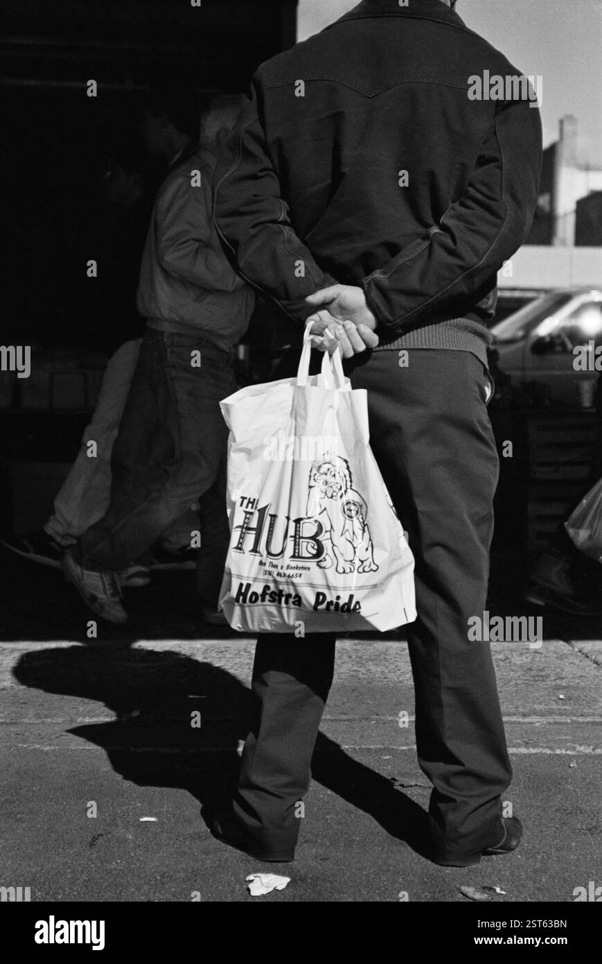 Schwarz-weiß monochromer vertikaler Mann, der die Tasche in der Hand auf dem Rücken hält und dunkle Kleidung trägt Stockfoto
