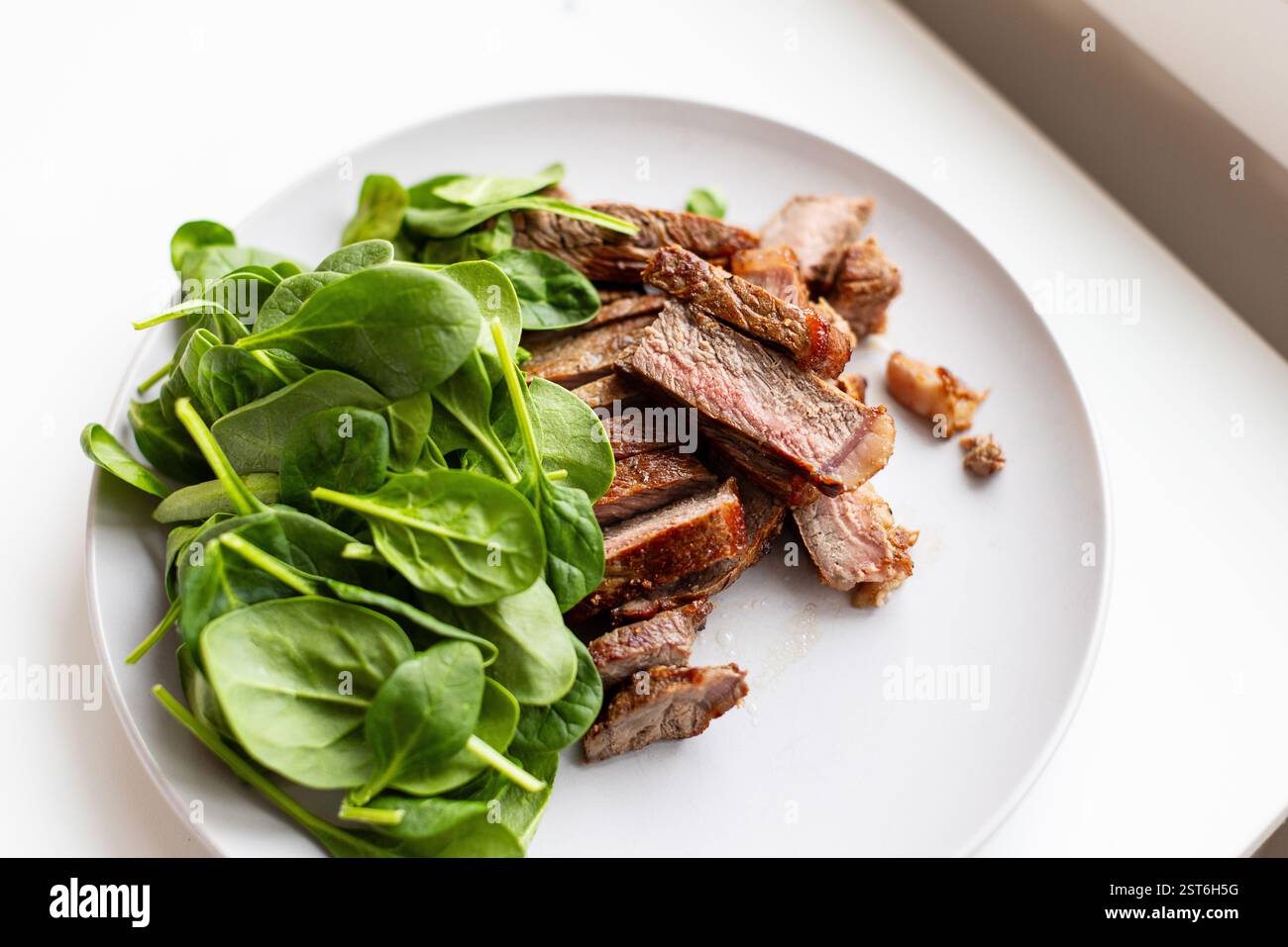 Teller mit Fleisch und Spinat. Das Fleisch wird in kleine Stücke geschnitten Stockfoto