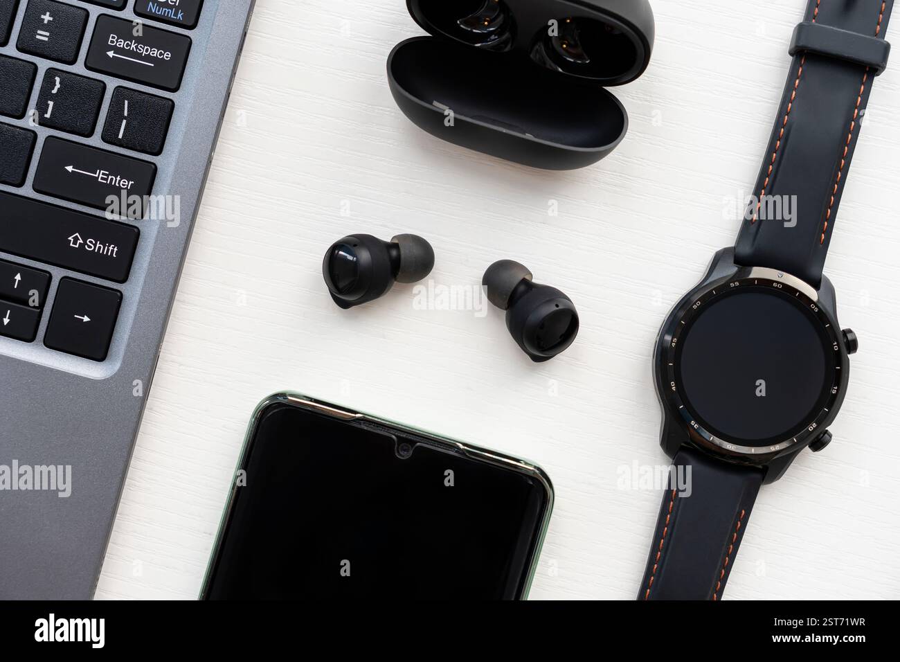 Ein Laptop, eine Smart Watch, Kopfhörer und ein Smartphone auf einem Holztisch. Stockfoto