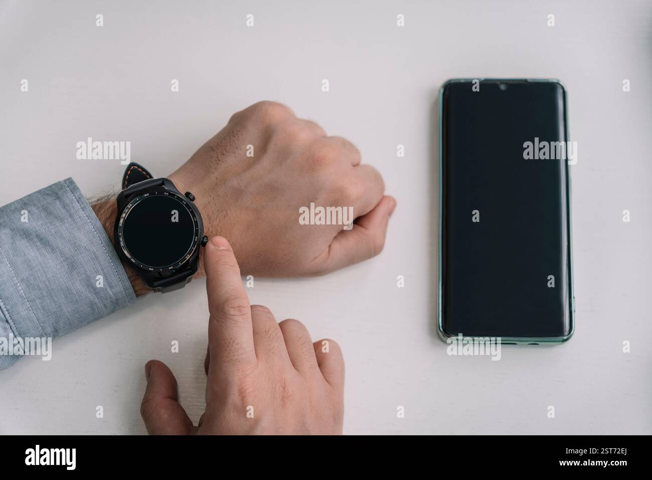 Ein Mann hält ein Smartphone und eine Smartwatch in der Hand. Kabellose Verbindung von Uhr und Mobiltelefon. Wi-Fi-Anschluss für Smartphone und Smartwatch Stockfoto