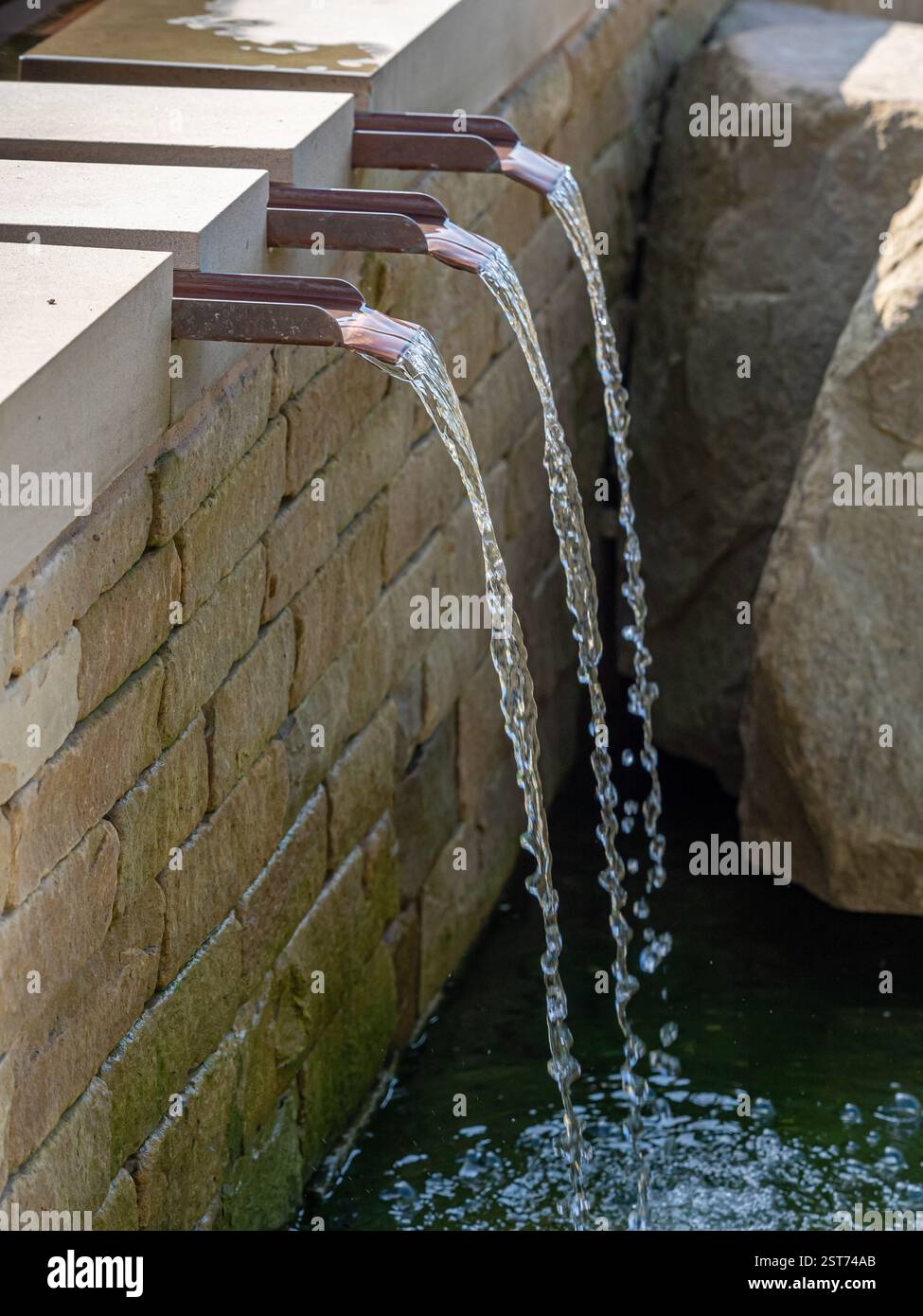Steinmauer mit drei schmalen Kanälen mit Kupferausläufen, die Wasser in einen Pool darunter gießen. Beningbrough Hall. York Stockfoto