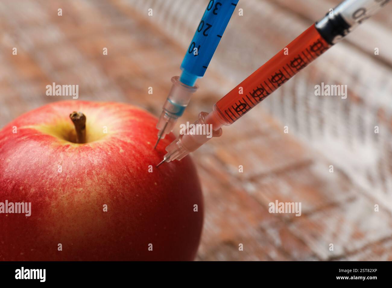 GVO-Konzept. Roter Apfel mit Spritzen auf verschwommenem Hintergrund, Nahaufnahme Stockfoto