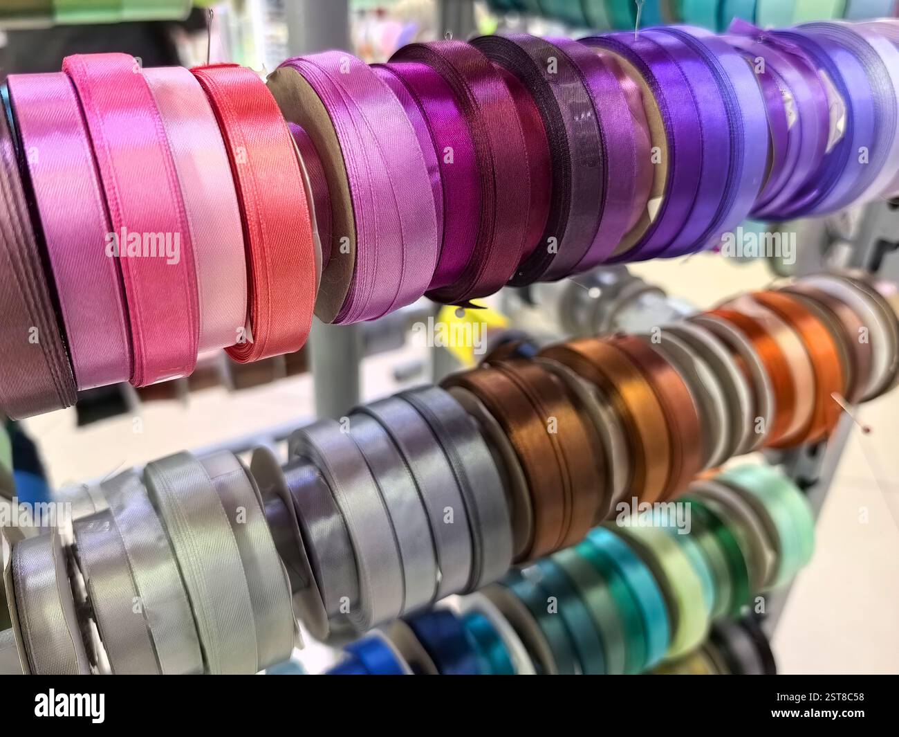 Ein lebendiges Display mit verschiedenen Satinbändern in verschiedenen Farben, ordentlich auf Spulen angeordnet. Der Laden ist hell und einladend, perfekt für Bastelbegeisterte Stockfoto