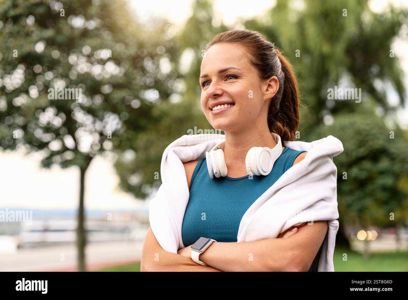 Porträt einer fitten jungen erwachsenen Frau mit Kopfhörern um den Hals, die draußen geht und lächelt Stockfoto