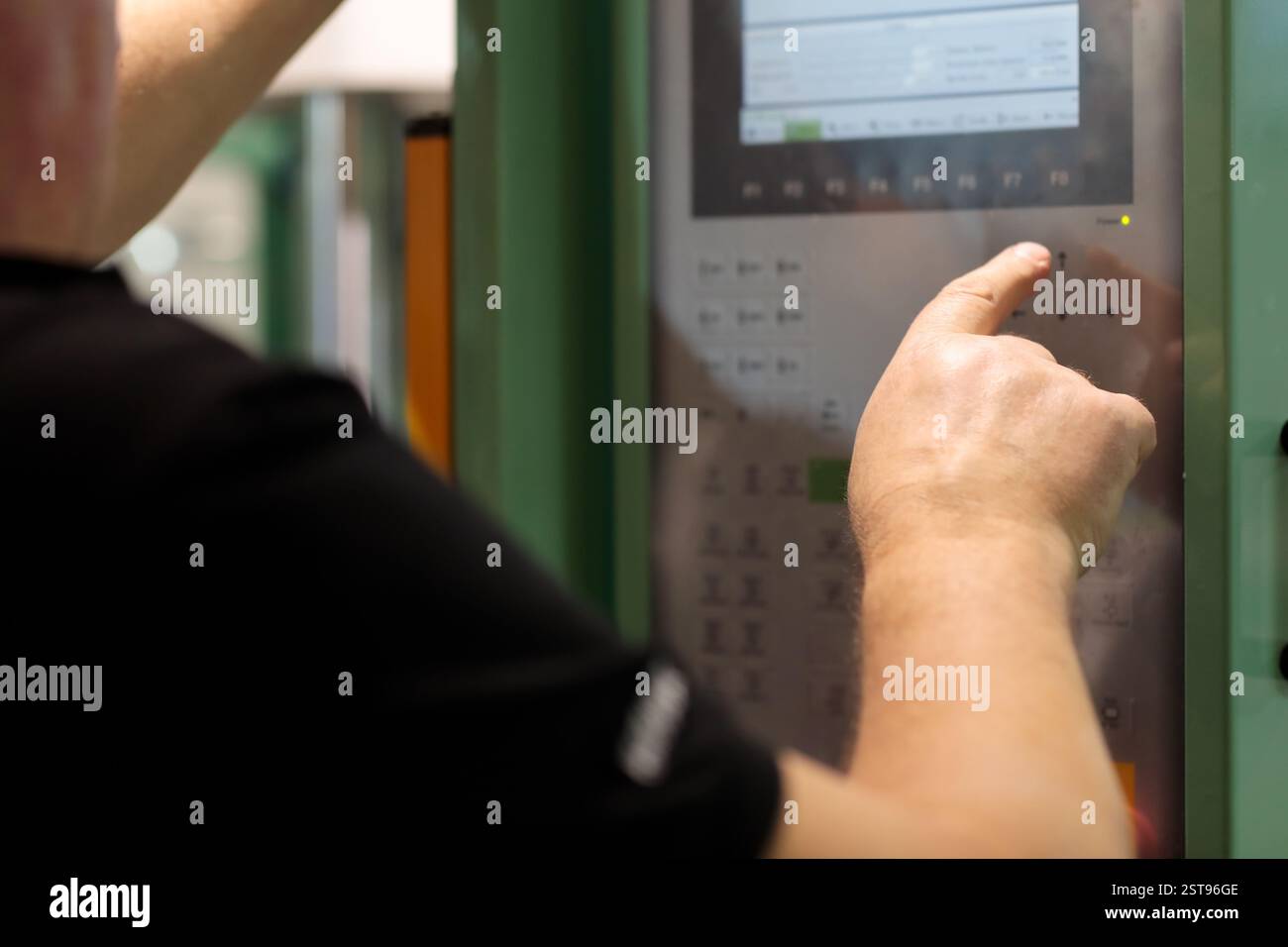 Der Fahrer steuert die Maschine mit dem Bedienfeld. Bediener der Kunststoff-Spritzgussmaschine bei der Arbeit. Modernes Industriekonzept. Auswahl Stockfoto