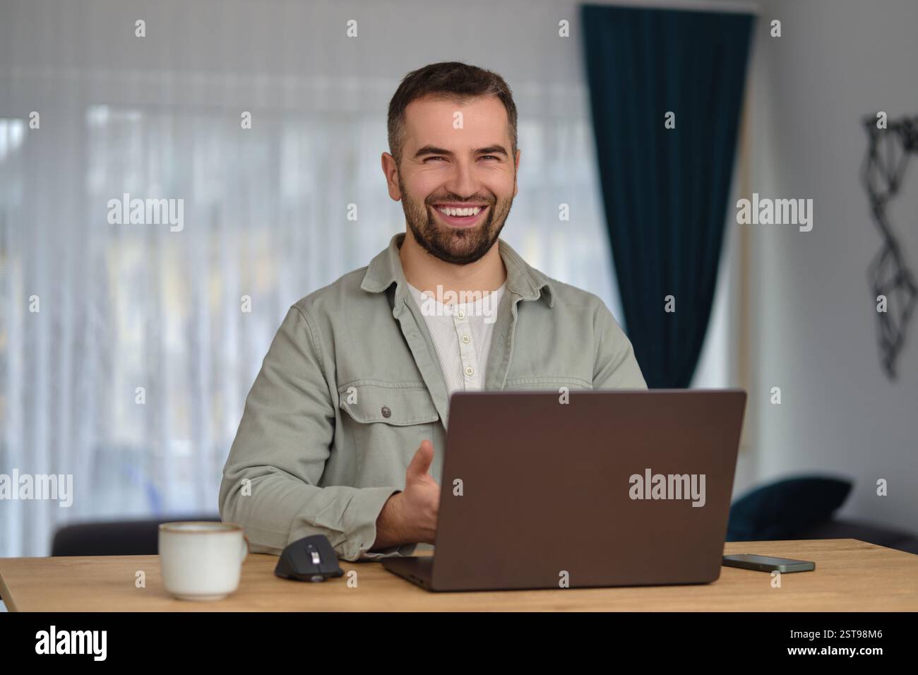 Ein glücklicher Mann, der einen Laptop benutzt, während er im Heimbüro arbeitet. Stockfoto