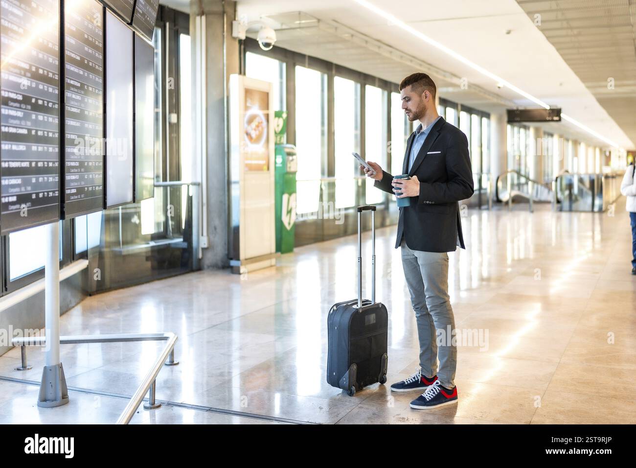 Geschäftsmann, der im Flughafenterminal mit Handy steht und Kaffee trinkt, während er auf seinen Flug wartet Stockfoto