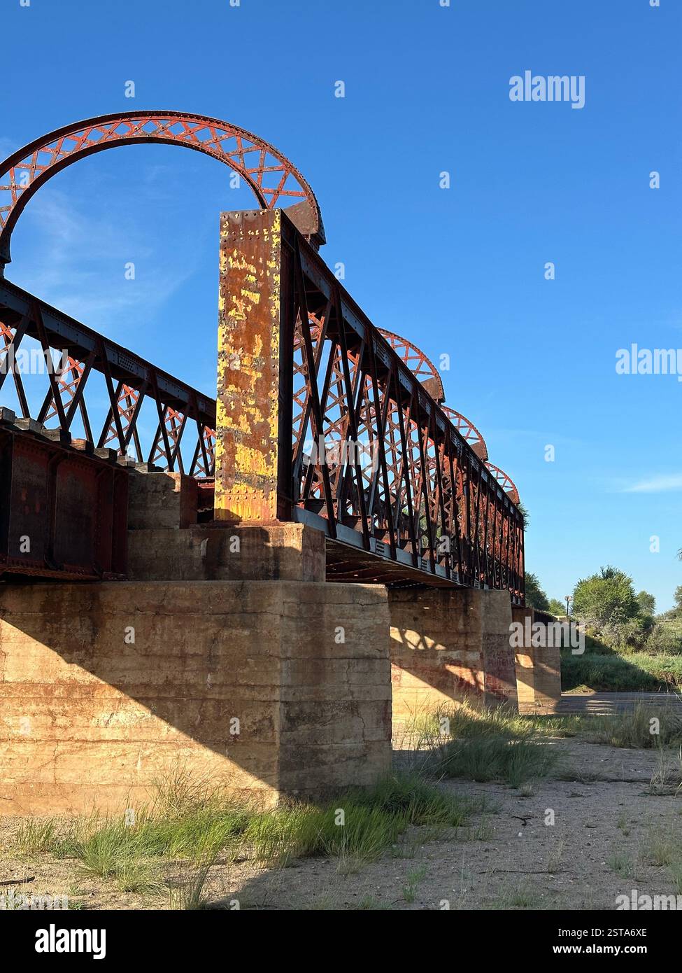 Eisenbahnbrücke aus rostigem Stahl mit verwitterten Betonstützen in einem trockenen Fluss, Seeis, Namibia - Smartphone-aufgenommenes Stockfoto
