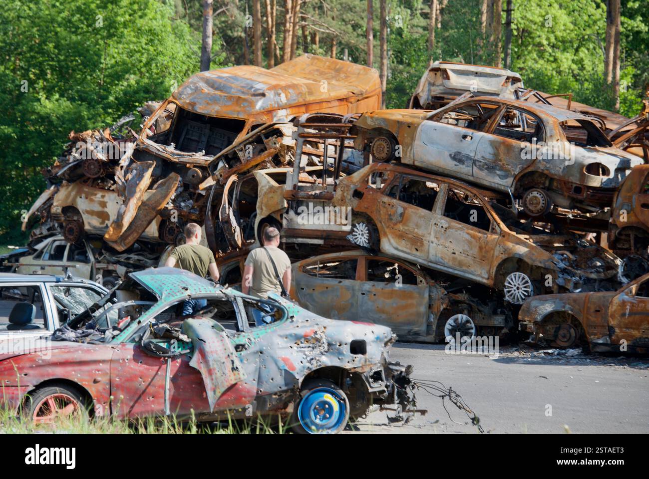 DIE BEWOHNER LAUFEN AM 8. JUNI 2022 DURCH EINEN AUTOFRIEDHOF, AUF DEM FAHRZEUGE, DIE VON RUSSISCHEN BOMBEN ZERSTÖRT WURDEN, IN DER NÄHE VON IRPIN IN DER UKRAINE. Stockfoto