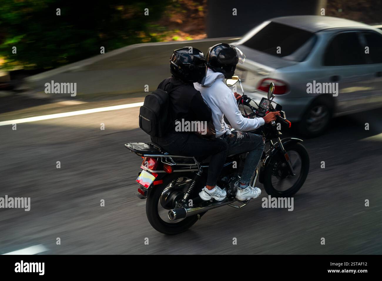 Ein Mann und eine Frau auf einer schwarzen Motorradfahrt durch die Stadt Caracas in Venezuela. Lifestyle. Ein Motorradfahrer fährt auf Stadtstraßen. Stadtleben. Stockfoto Ein Mann und eine Frau auf einer schwarzen Motorradfahrt durch die Stadt Caracas in Venezuela. Lifestyle. Ein Motorradfahrer fährt auf Stadtstraßen. Stadtleben. Stockfoto