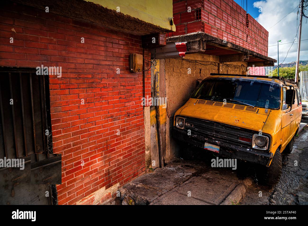 Eine Straße in lateinamerika. Arme Viertel in Cacas, Venezuela. Ein altes Auto parkte auf der Straße. Stockfoto Eine Straße in lateinamerika. Arme Viertel in Cacas, Venezuela. Ein altes Auto parkte auf der Straße. Stockfoto